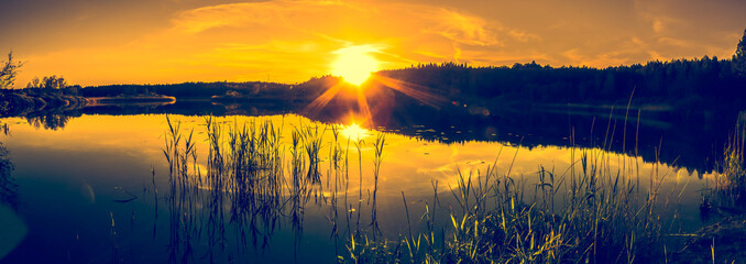Summer landscape with sunset on the lake. Beautiful orange sundown or sunrise over forest and peaceful water with reflection of sun light, warm scenery in nature.