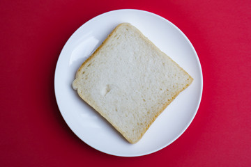 Fototapeta na wymiar A slice of toast on a white plate, red background