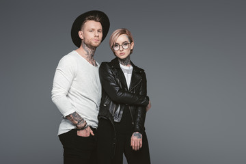 stylish tattooed couple posing together, isolated on grey