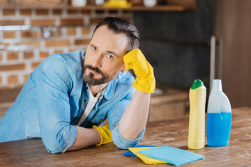 Boring cleaning. Attractive reflective male cleaner leaning on his hand while wearing gloves and gazing at the camera