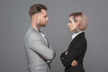 stylish businessman and businesswoman with crossed arms looking at each other, isolated on grey