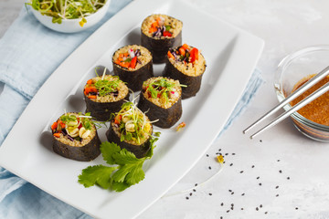 Vegan sushi rolls with quinoa, vegetables and soy-nut sauce on a white plate, light background....