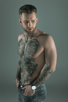handsome shirtless tattooed man with hands in pockets, isolated on grey