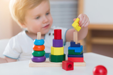 Two years old child boy playing with wooden colorful blocks and sorting shapes at home. educational toys concept. Development of kids fine motor skills, imagination and logical thinking