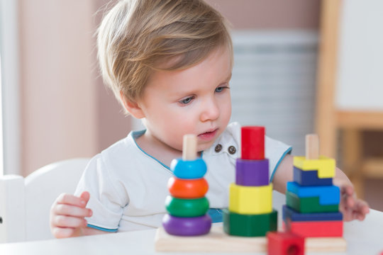 Two years old child boy playing with wooden colorful blocks and sorting shapes at home. educational toys concept. Development of kids fine motor skills, imagination and logical thinking