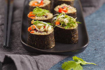 Vegan sushi rolls with quinoa, vegetables and soy-nut sauce on a black plate, black background. Vegan Healthy Food Concept.