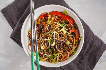 Healthy vegan buckwheat noodles with a mix of vegetables, sprouts and nut-soy sauce. Vegetarian padthai soba noodles in white bowl on gray background. Top view