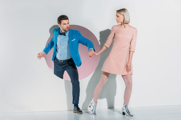 young couple in suit and dress holding hands and looking at each other on grey