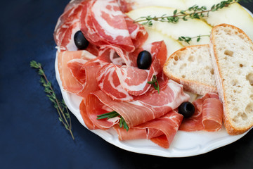 Italian antipasto, melon, thyme and olives on a plate close-up