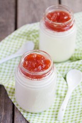 Homemade yogurt with apple jam in two small glass jars on a wooden table with green cloth, selective focus