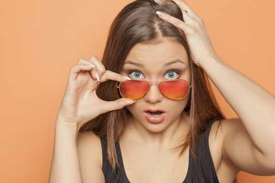 young strartled girl with orange sunglasses on orange background