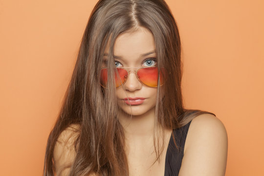 young beautiful girl with orange sunglasses on orange background