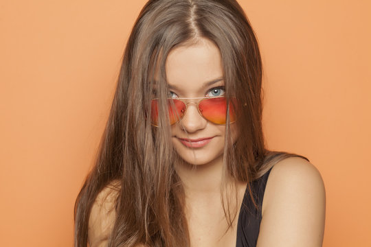 young smiling girl with orange sunglasses on orange background