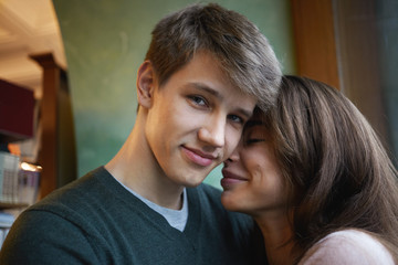 Close up picture of pretty girl with cute smile and stylish clean shaven young male cuddling at home, having happy looks, enjoying each other's company. Love, relationships and happiness concept
