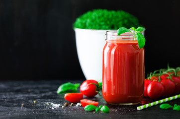 Organic fresh tomato juice in a glass jar, basil, cherry, salt, pepper and straw on dark black background. Clean eating and diet concept. Copy space