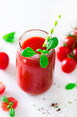 Organic fresh tomato juice in a glass jar, basil, cherry, salt, pepper and straw on light background. Clean eating and diet concept. Copy space.