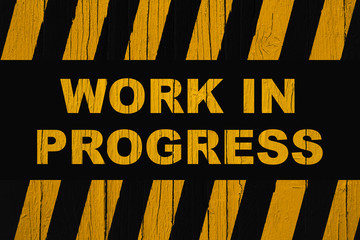 Work in progress warning sign with dark yellow orange and black stripes painted over cracked wood.