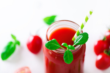 Organic fresh tomato juice in a glass jar, basil, cherry, salt, pepper and straw on light background. Clean eating and diet concept. Copy space.