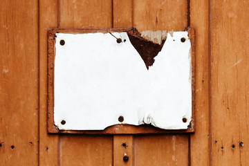 Empty rusty cracked and grungy white sign in rectangular shape weathered under the elements and fixed to an old red brown wooden wall with rusty nails