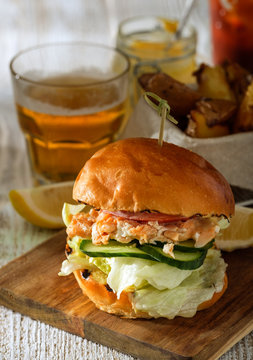 Fishburger with toppings, fries  and a glass of beer. Rustic style