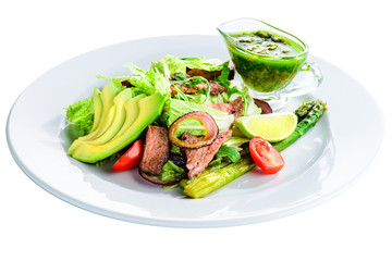 Delicious green meat salad with roasted juicy steak, avocado and green sauce in a white plate isolated on white background