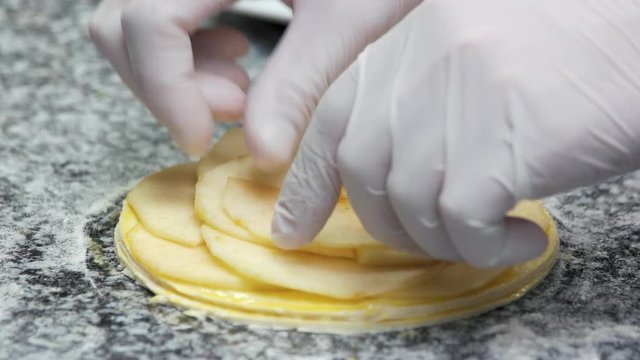 Chef put apple slices one by one. Close up chef hands making apple tart layers.