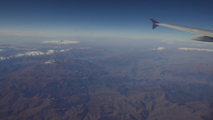 Mountain range from the airplane window. Airplane wing. Aerial view on mountains through window of an aircraft. Mountain from the airplane window. Travel concept.