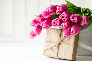 Violet tulips bouquet in basket in front of white wooden wall. Space for copy