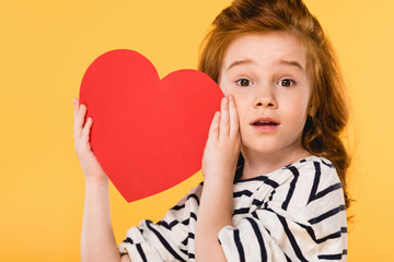 portrait of shocked child with red paper heart isolated on yellow, st valentines day concept