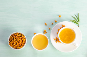 Sea buckthorn in porcelain bowl, honey and cup of  tea with Sea buckthorn on blue table. top view