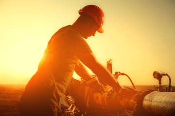 Oil worker is checking the oil pump on the sunset background.