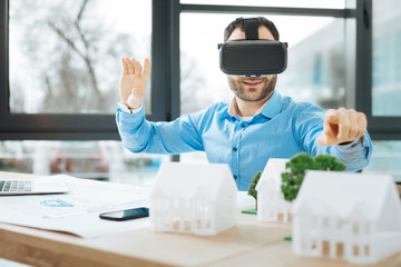 New project. Charming young architect sitting at the work desk, wearing a VR headset and pointing...