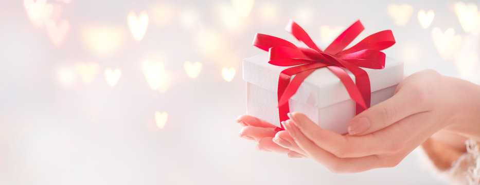 Valentine's Day. Woman holding gift box with red bow over holiday background