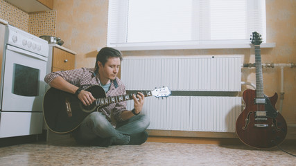 Young man composes music on the guitar and plays in the kitchen, other musical instrument in the...