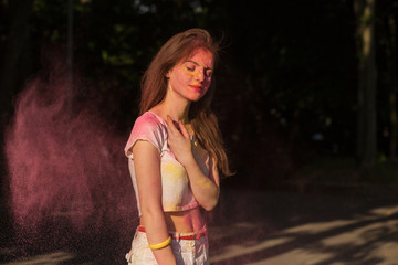 Charming young woman posing with pink powder Holi exploding around her