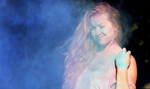 Lovely young woman with curly hair posing in a cloud of blue powder at Holi festival of colors