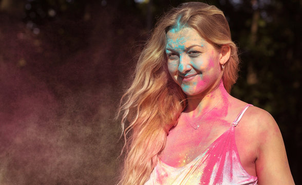 Closeup portrait of smiling blonde model covered with colorful dry paint at Holi festival of colors
