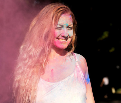 Happy blonde model with curly hair playing with pink dry paint Holi at the park