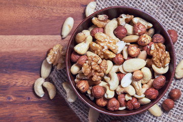 Mixed nuts including hazelnuts, walnuts, blanched almonds and cashews in wooden bowl. Top view with copy space