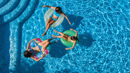 Aerial top view of family in swimming pool from above, happy mother and kids swim on inflatable ring donuts and have fun in water on family vacation

