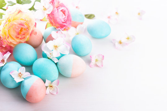 Easter and flowers background, spring concept. Blue and pink chicken eggs on white wooden table, pastel colors