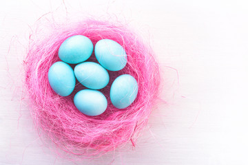 Easter eggs in a pink nest. Blue or turquoise chicken eggs on white wooden background