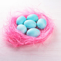 Fototapeta na wymiar Easter eggs in a pink nest. Blue or turquoise chicken eggs on white wooden background