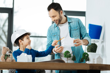 Obraz premium Nice suggestion. Loving young father offering a toy house for the bear of his son while the boy in a hard hat pointing at it and smiling