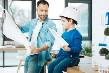 Skilled artists. Cute little boy in a white hard hat holding a picture while sitting on the table...