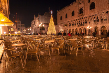 Fototapeta na wymiar VENICE, ITALY - JANUARY 02 2018: night view of chairs and tables of a bar in Piazza San Marco with the Christmas tree in the background