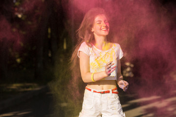 Obraz premium Lovely brunette model having fun in a cloud of yellow and pink dry paint at Holi festival