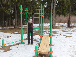 Adult woman in a brown jacket training on a horizontal bar on a street sports field in the autumn forest