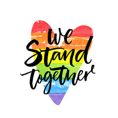 We stand together. Inspirational LGBT slogan han dwritten on rainbow flag heart.