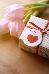 Geschenk mit Herz und rosa Tulpen im Sonnenlicht